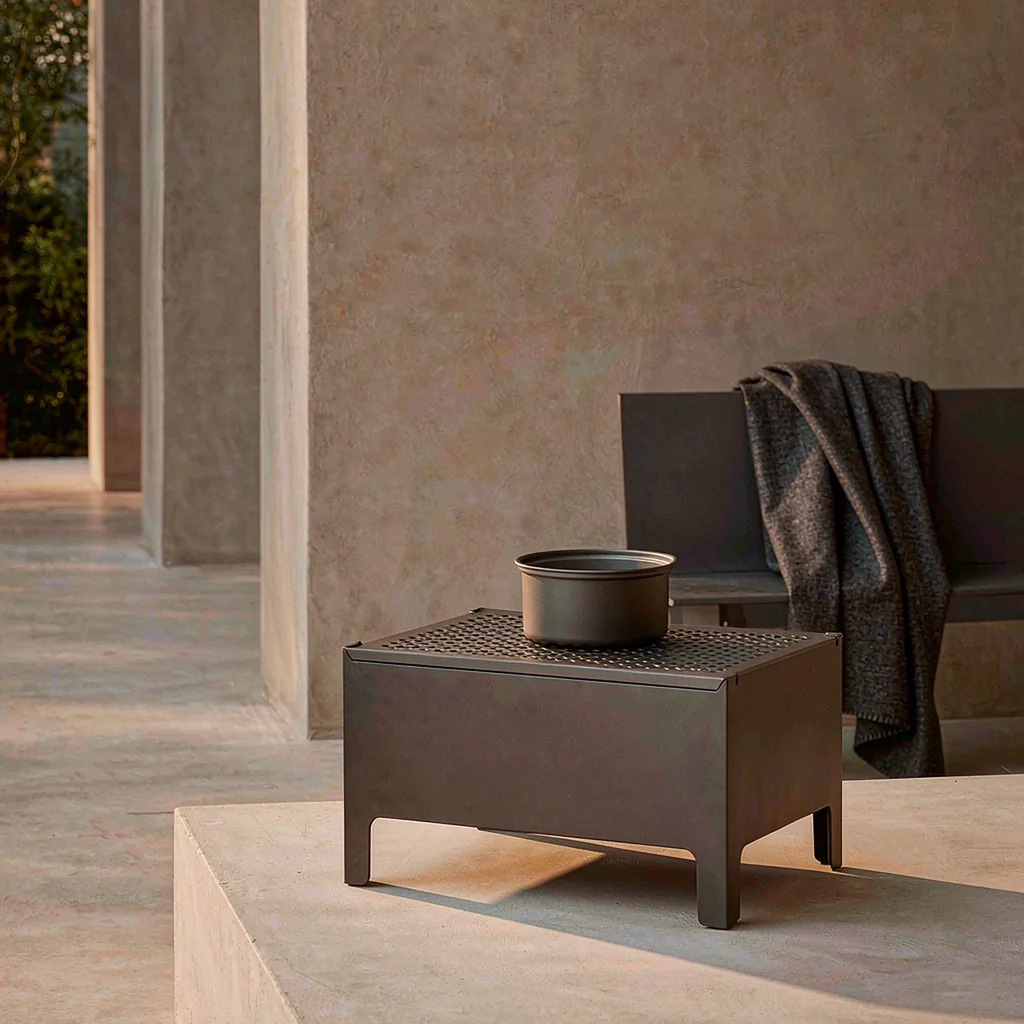 Compact two-in-one outdoor radiant heater and cooking stove on a stone terrace at dusk