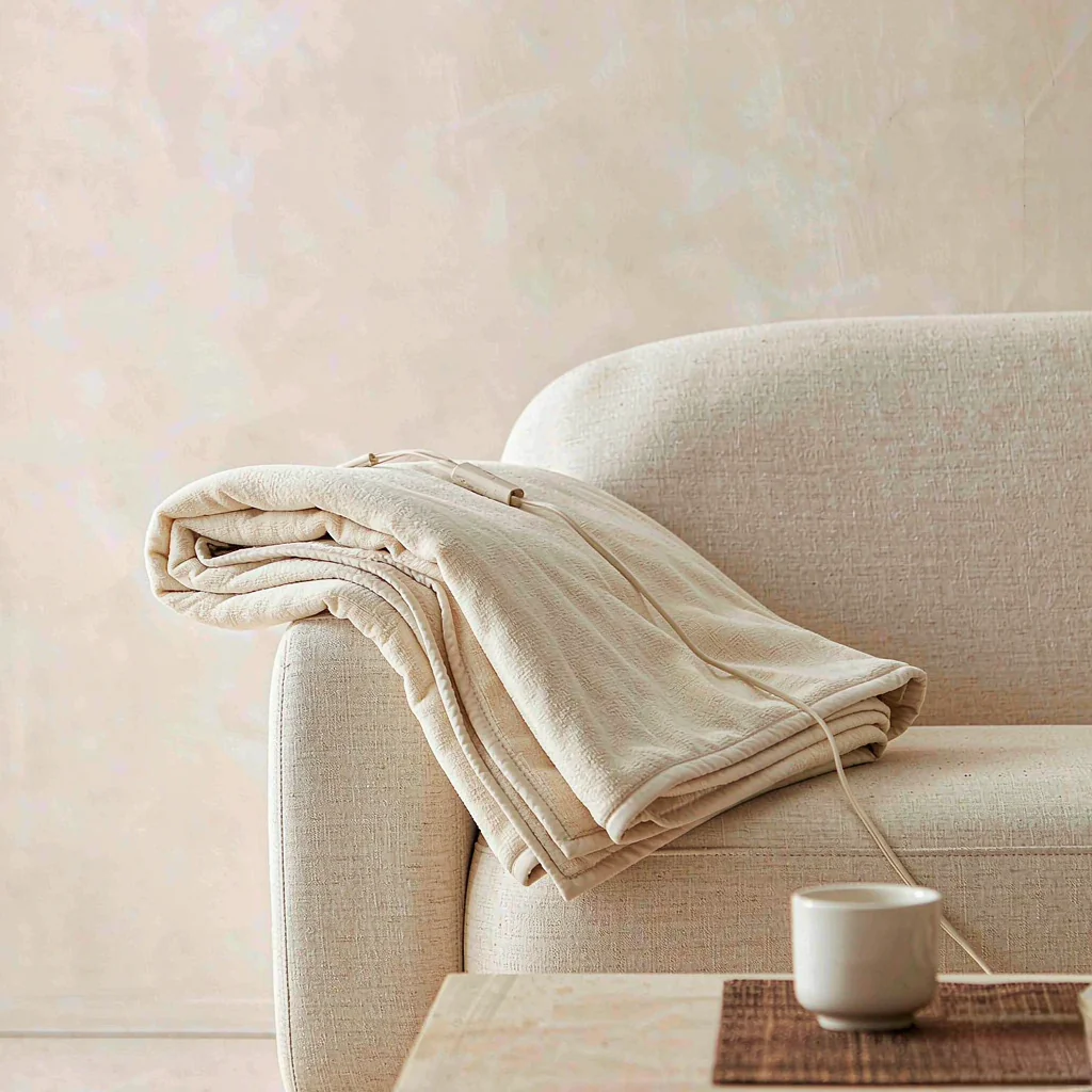 Folded oatmeal faux-fur heated throw draped over a linen sofa arm